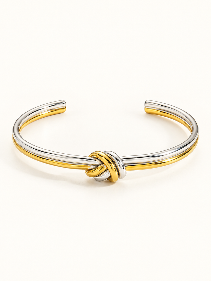 Gold-tone and silver-tone double-line open cuff bracelet with a single central knot on an ivory background